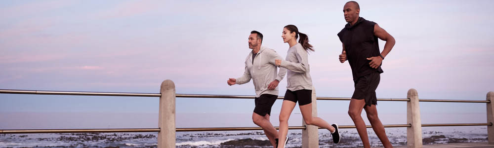 2 young men and a woman running along a waterfront path near sunset